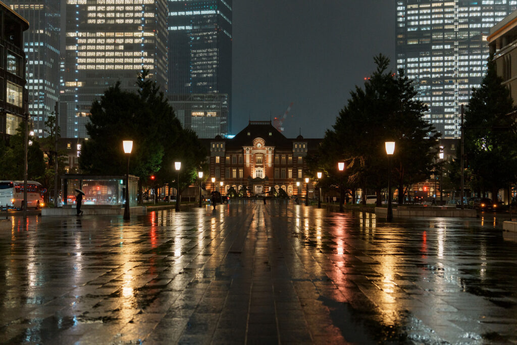 Night city skyline with tall skyscrapers and reflections on wet streets, captured with Tamron 35-100.