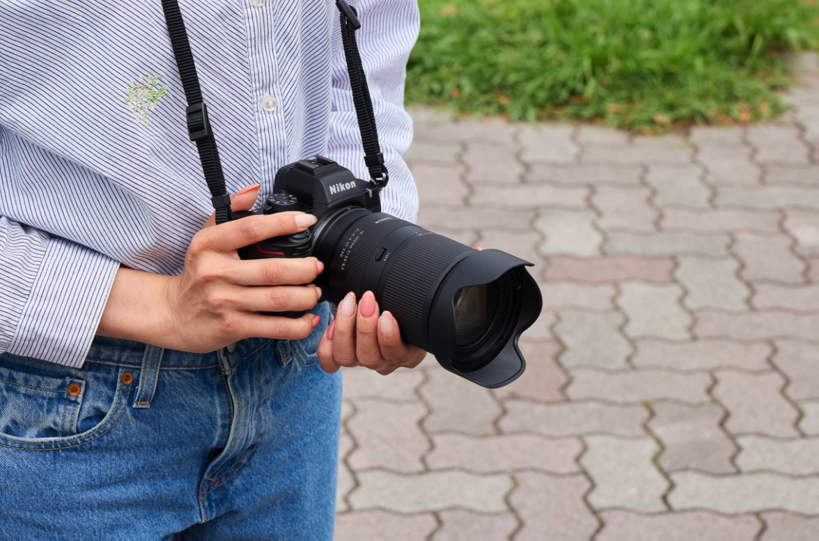 Tamron Lens in Use for Photography Person holding a Nikon camera with Tamron lens outdoors.