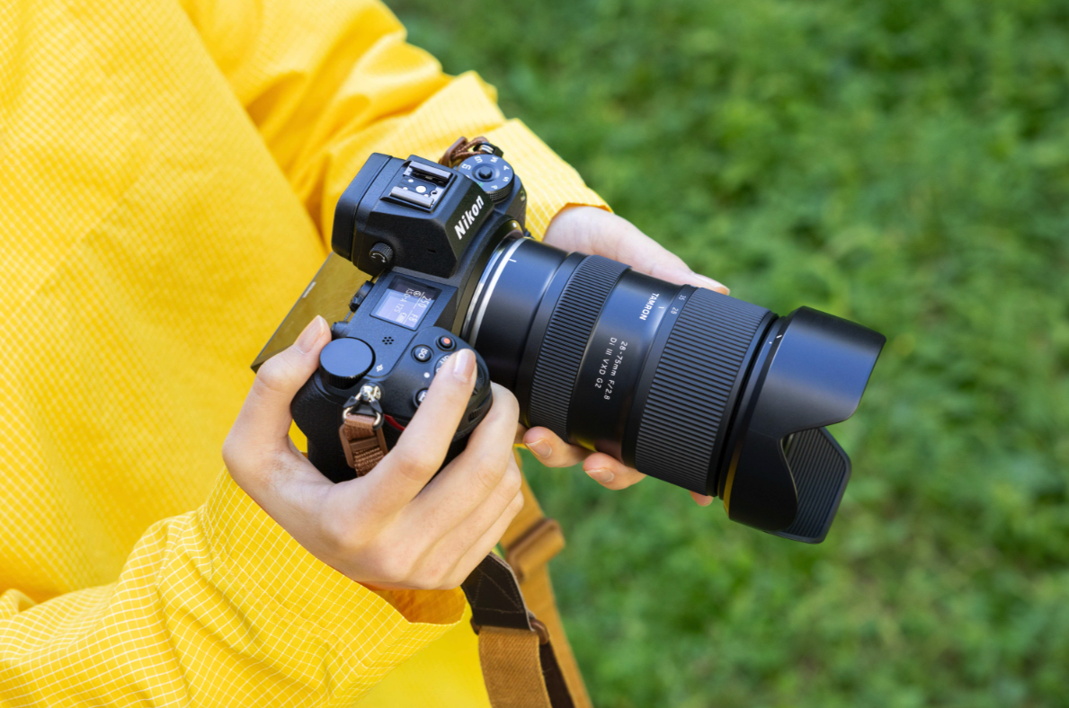Person holding a Nikon camera with a Tamron lens outdoors.