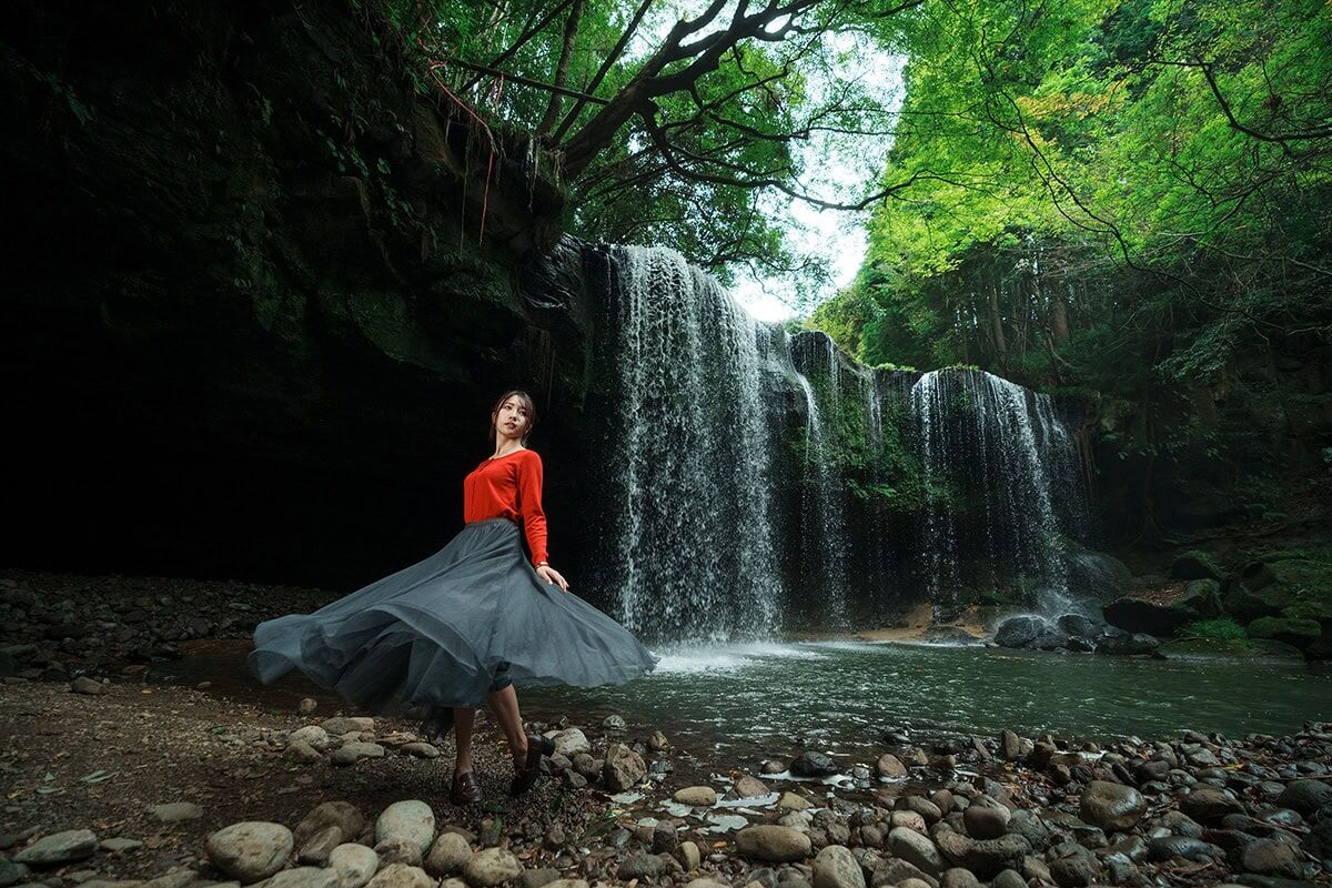 Photo taken with a Tamron lens of a woman near a waterfall in lush forest.