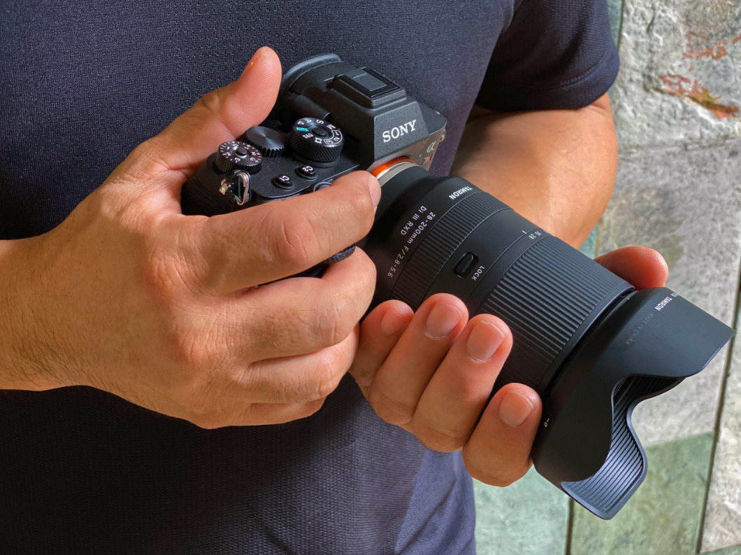 Tamron camera lens with Sony camera in hand Tamron lens attached to Sony camera held by a person.