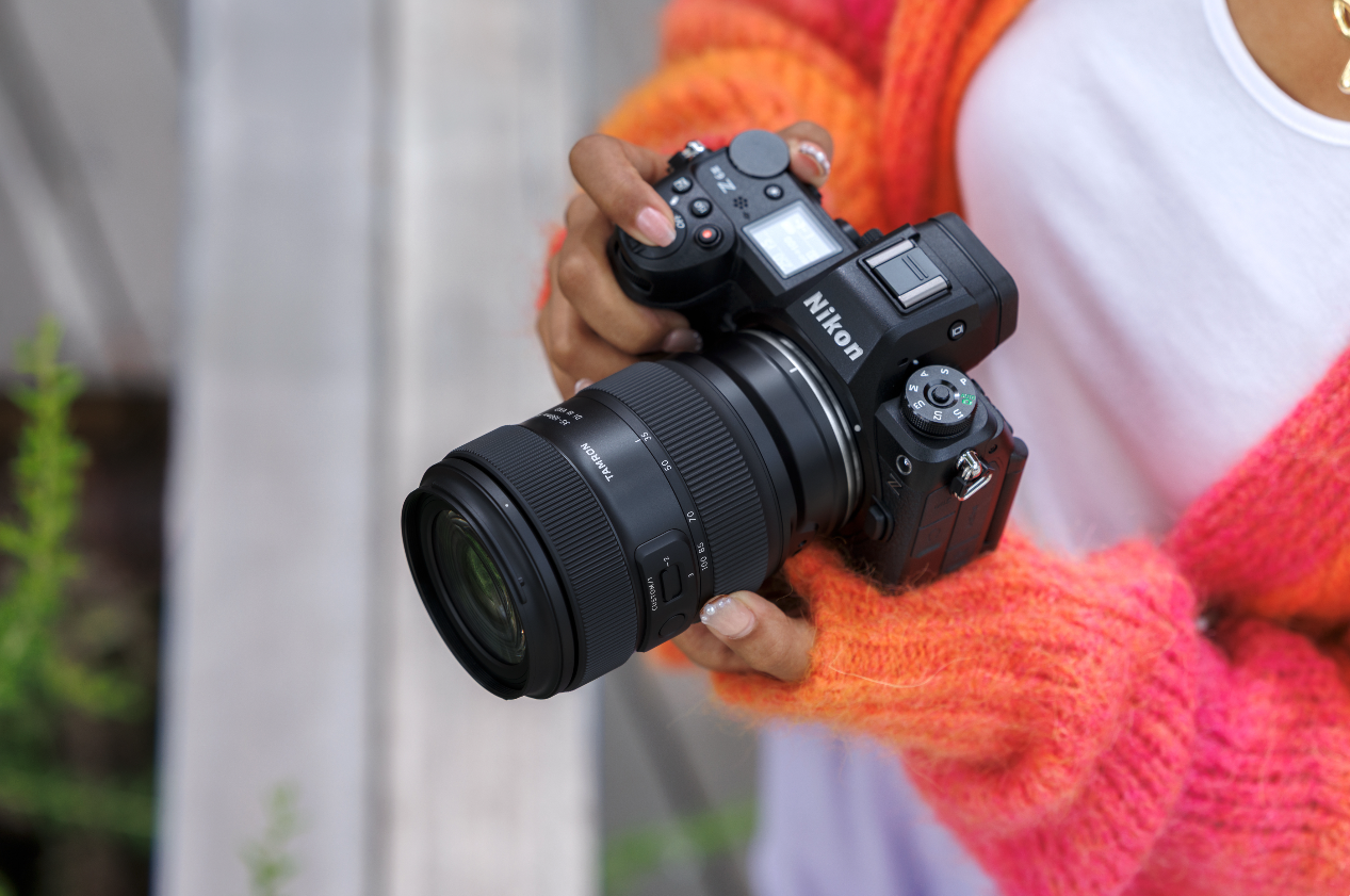 Tamron Australia camera gear Person holding a Nikon camera with Tamron lens outdoors.