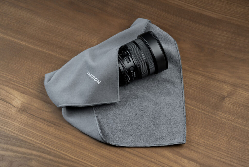 Tamron camera lens with cleaning cloth on wooden surface.