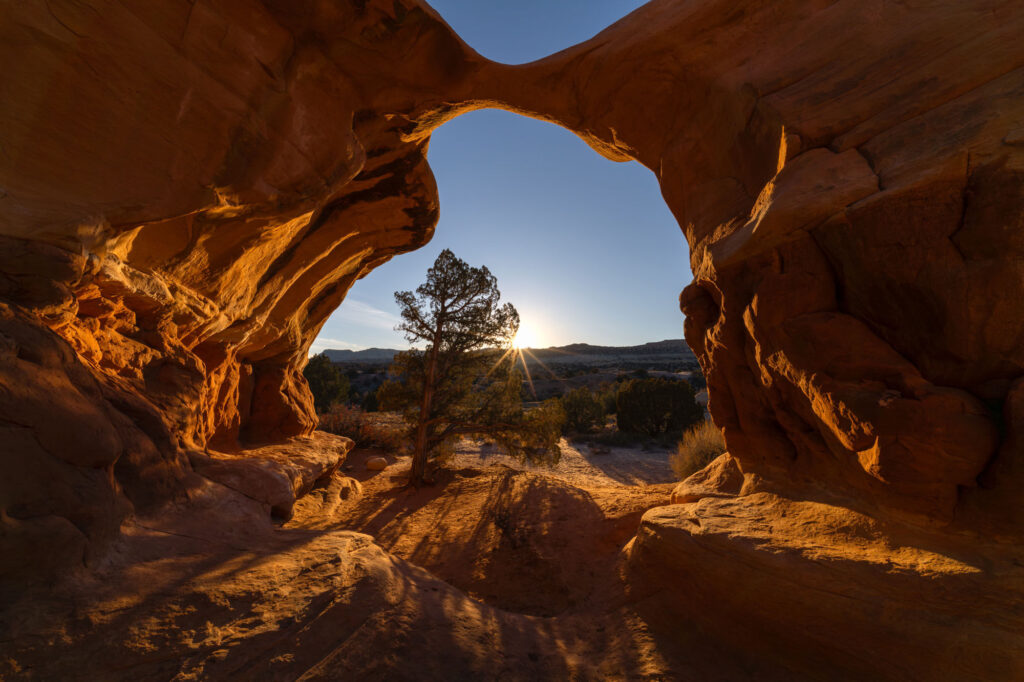 Sunset view through a natural desert rock arch in a rugged landscape.