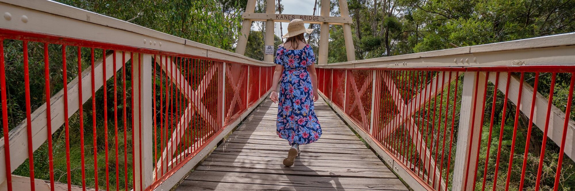Woman in floral dress walking on a red bridge, taken with a Tamron lens.