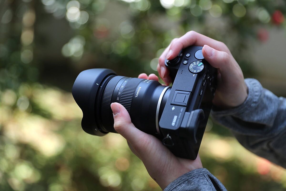 Person holding a camera with a Tamron lens outdoors.