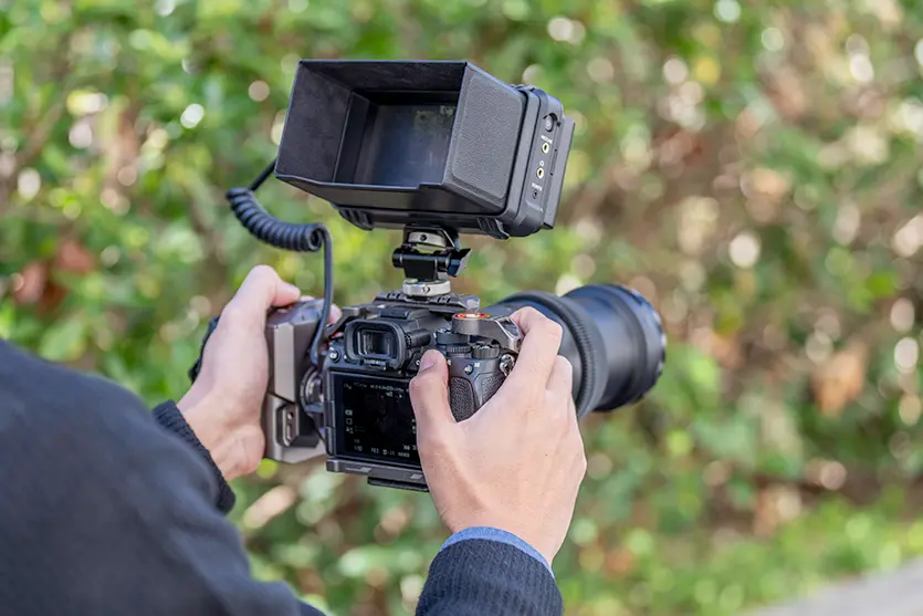 Photographer holding a camera with a Tamron lens outdoors.