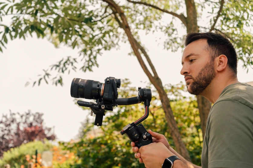 Man using a Tamron lens on a camera outdoors in nature.