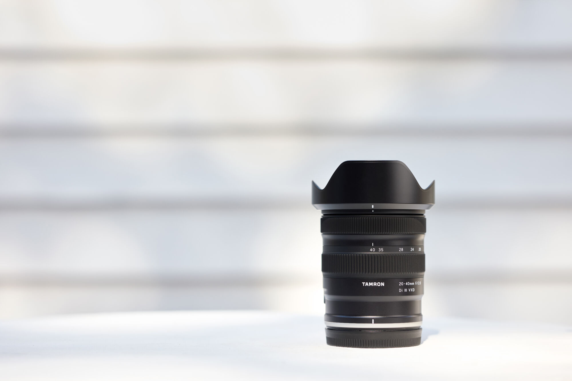 Tamron 12-20mm F/2.8 lens on a white surface with blurred background.